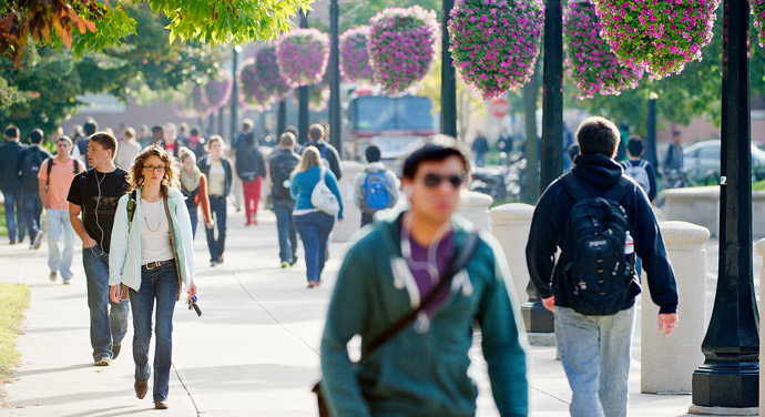 a crowd of students walking through memorial mall on the Purdue campus with hanging flower baskets and fall foliage