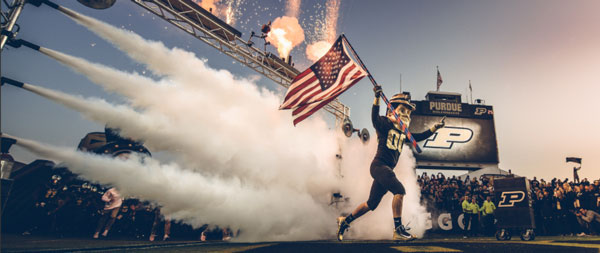 Purdue Pete running onto the field holding the American flag