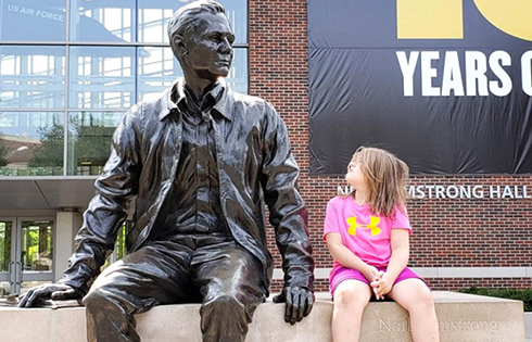 child sits by and looks up at Neil Armstrong statue